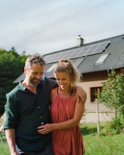 Happy couple standying near their house with solar panels. Alternative energy, saving resources and